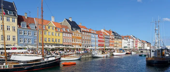 Nyhavn on a sunny day: painted townhouses in yellow, red and blue along the canal quay, with old wooden sailing ships moored in the foreground
