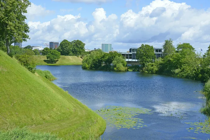 The grassy rampart of Kastellet sloping down to its moat, with trees and lily pads on the still water