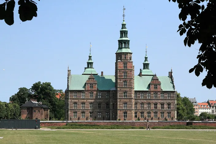 Rosenborg Castle's red-brick Renaissance facade and green copper towers seen across the lawn of the King's Garden under a blue sky