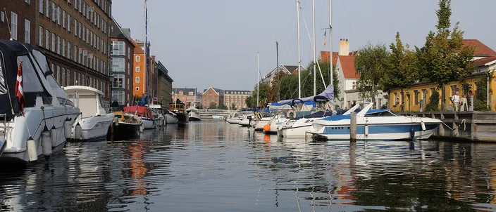 Christianshavn's canal on a calm day, motorboats and sailing masts moored along both quays and old brick warehouses reflected in the water
