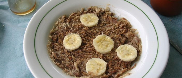 A shallow plate of dark shredded beef spread over manioc flour, topped with five slices of banana