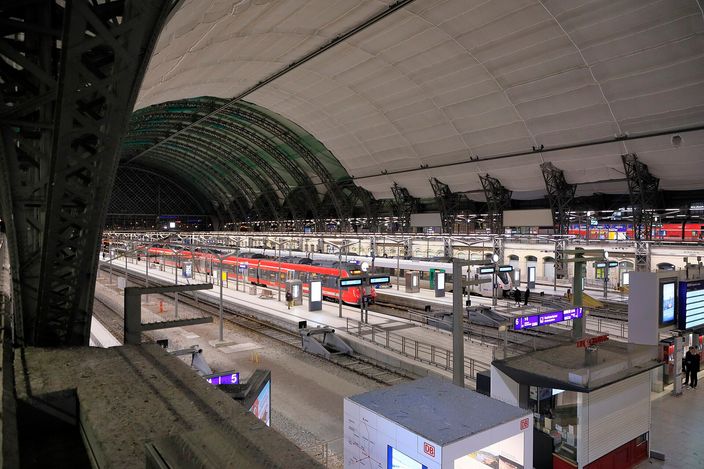 Interior of Dresden Hauptbahnhof under its curved translucent membrane roof, with red double-deck regional trains standing at platforms and steel arches spanning overhead