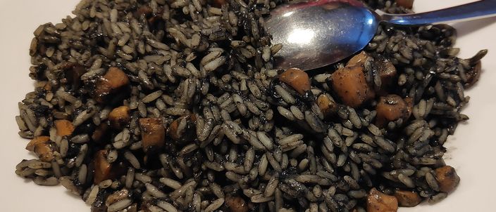 A mound of glistening jet-black risotto studded with tender pieces of cuttlefish, served on a white plate with a spoon.
