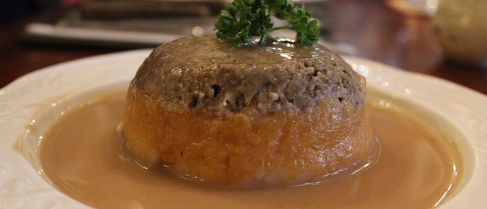 A plated serving of haggis with mashed neeps and tatties, finished with a pour of sauce and a sprig of parsley