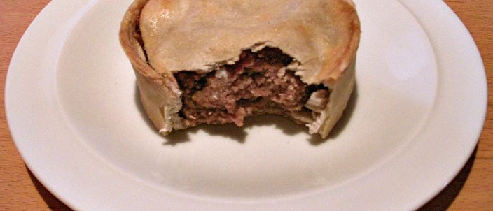 A Scotch pie on a white plate with a bite taken out, showing the mutton filling and the straight pastry wall