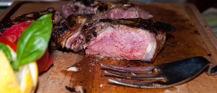 A thick bone-in Florentine steak, sliced to show its rare red centre, resting on a wooden board with a sprig of basil.