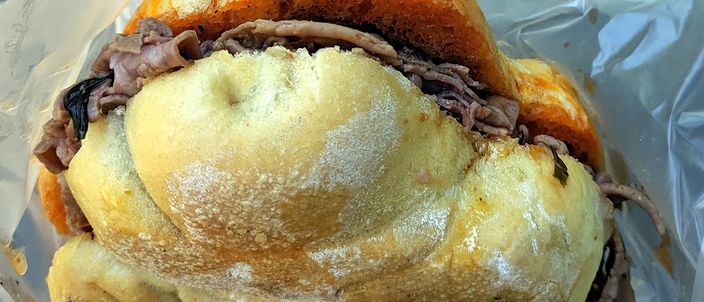 A lampredotto sandwich — chopped tripe piled into a round bread roll — held in its paper wrapping.