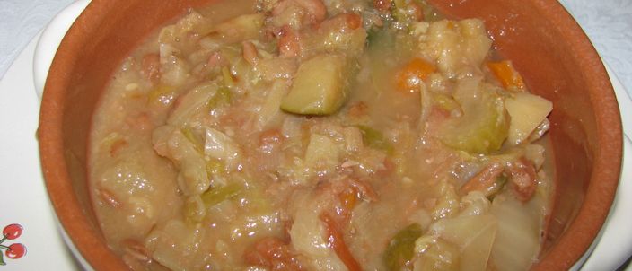 A terracotta bowl of ribollita: a thick, mounded mash of bread, cavolo nero, cabbage and beans with carrot pieces, no free liquid, on a white plate