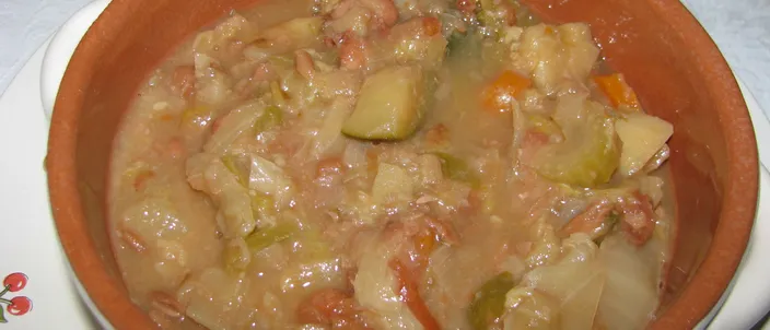 A terracotta bowl of ribollita: a thick, mounded mash of bread, cavolo nero, cabbage and beans with carrot pieces, no free liquid, on a white plate