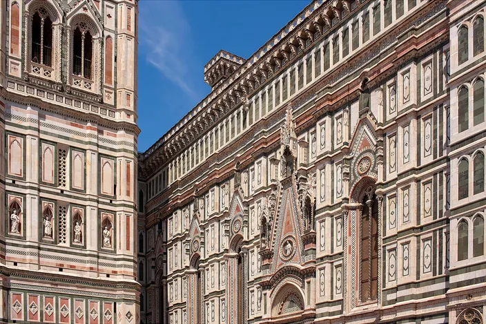 The south flank of Florence Cathedral in green, white and pink striped marble standing immediately beside the equally striped bell tower, the two facades almost touching under a clear blue sky
