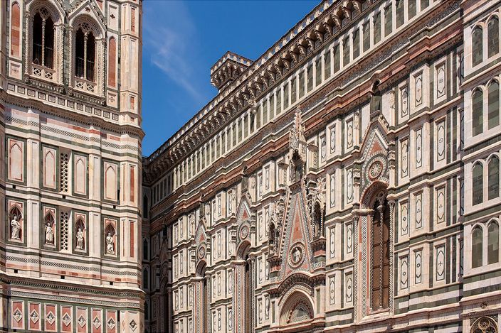 The south flank of Florence Cathedral in green, white and pink striped marble standing immediately beside the equally striped bell tower, the two facades almost touching under a clear blue sky