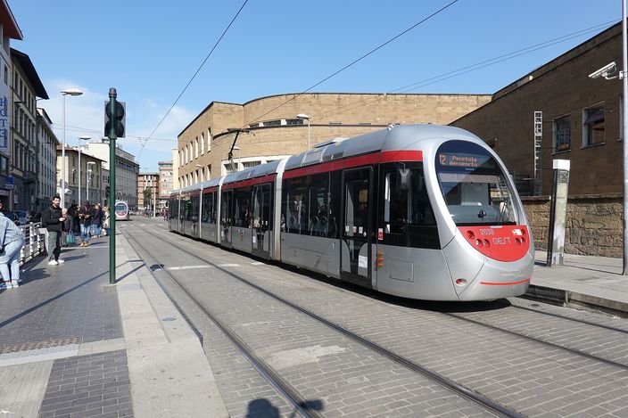 A silver and red Florence tram signed T2 Peretola Aeroporto standing at a street-level stop beside the station, with passengers waiting on the platform
