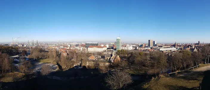 Wide winter panorama of Gdańsk from the green slopes of Gradowa Hill, with the Main Town's roofs, towers and the city skyline stretching to the horizon under a clear blue sky.