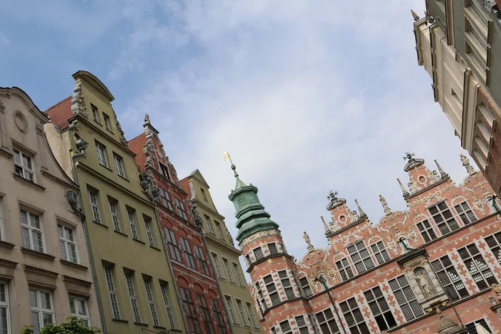 Ornate Dutch-Renaissance gables of the Great Armoury in red brick and pale stone, beside colorful pastel townhouses on Ulica Piwna, seen against a blue sky with light cloud.