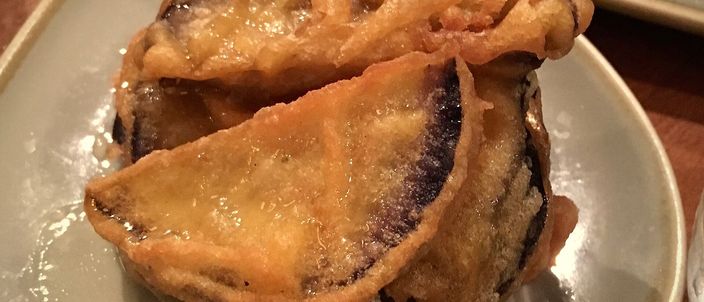 A plate of berenjenas con miel: wedges of aubergine in a crisp golden batter, glossy with a dark syrup drizzle.