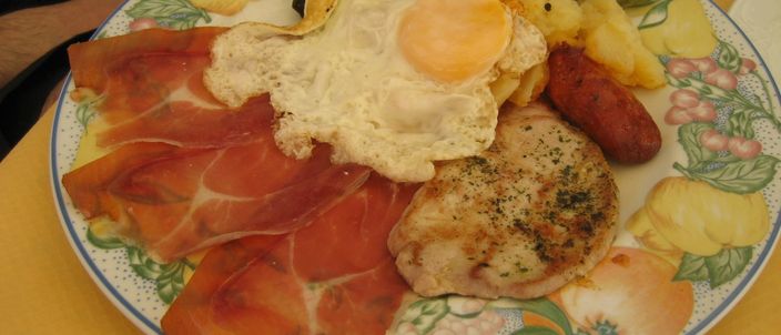 A large plate of cured ham, fried egg, potatoes, black pudding and sausage, seen from above
