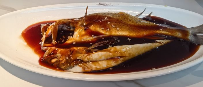 A whole vinegar-glazed grass carp, split lengthwise, plated on an oval white dish with a thin, glossy reddish-brown sauce pooling around the fish rather than coating it thickly.