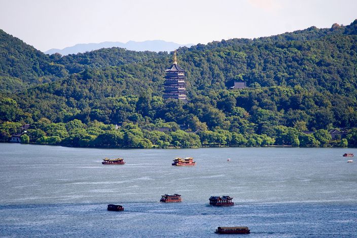 Leifeng Pagoda rising above the treeline on West Lake's far shore, seen across open water with a handful of red pleasure boats in front of it.
