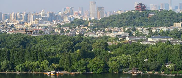 Hangzhou's skyline and West Lake seen from Wu Hill, with the red-roofed City God Pavilion among the trees on the right.