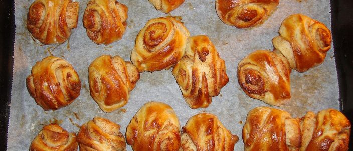 A tray of freshly baked korvapuusti cinnamon buns, golden and glossy, each pressed into the splayed ear shape.