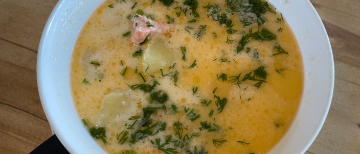 A white bowl of creamy salmon soup with chunks of salmon and potato and a scatter of fresh dill.