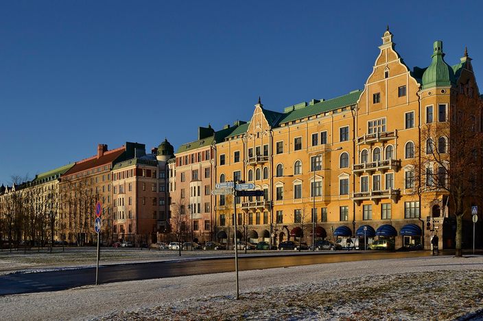 A terrace of ornate Jugend apartment houses with green copper roofs and stepped gables along a wide street in low winter sun, deep blue sky above, patches of snow on the verge and almost nobody about.