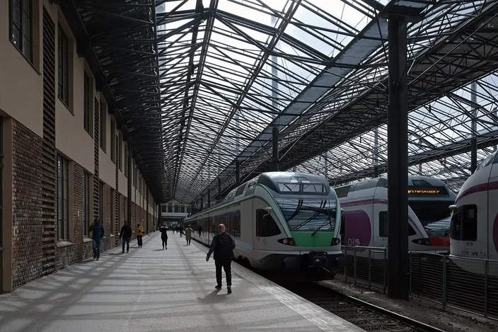 Green-and-white commuter trains standing at platforms beneath the arched steel-and-glass train shed of Helsinki Central Station, a lone figure walking down the platform