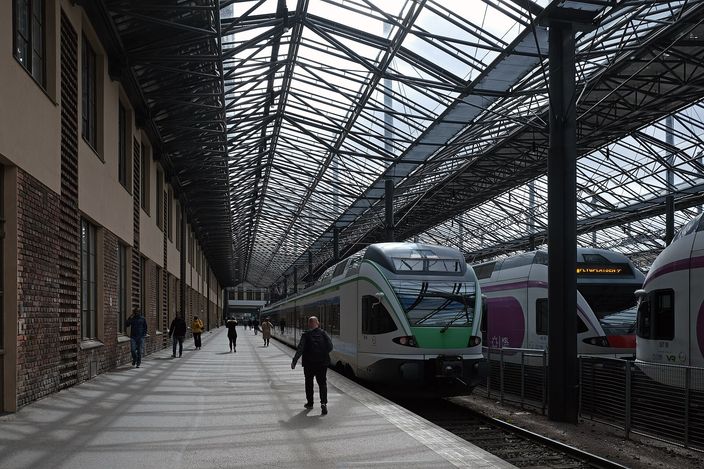 Green-and-white commuter trains standing at platforms beneath the arched steel-and-glass train shed of Helsinki Central Station, a lone figure walking down the platform