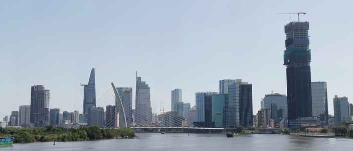 The Ho Chi Minh City skyline seen across the Saigon River in daylight: the cylindrical Bitexco Financial Tower with its helipad, the cable-stayed Thu Thiem 2 (Ba Son) bridge, clustered District 1 high-rises and the tall Landmark 81 tower under construction at right.
