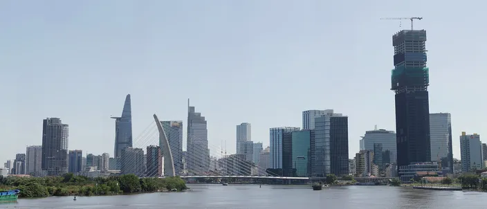 The Ho Chi Minh City skyline seen across the Saigon River in daylight: the cylindrical Bitexco Financial Tower with its helipad, the cable-stayed Thu Thiem 2 (Ba Son) bridge, clustered District 1 high-rises and the tall Landmark 81 tower under construction at right.