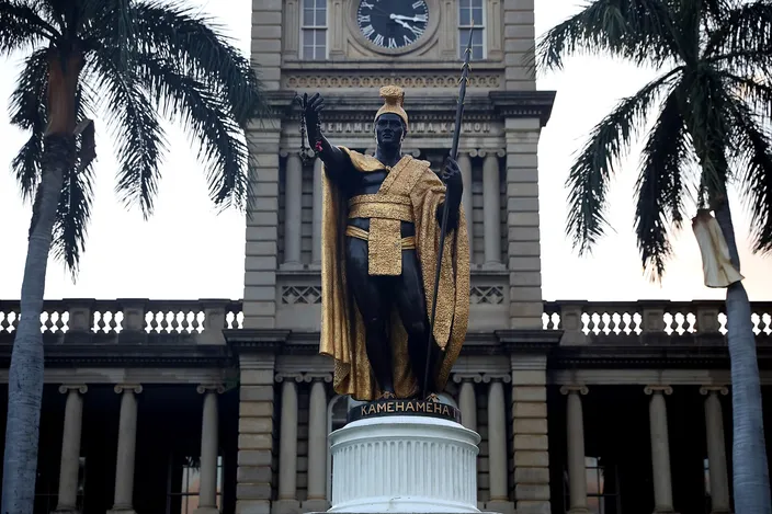 The gilded bronze statue of King Kamehameha with spear and feather cloak in front of the clock tower of Aliʻiōlani Hale, palms either side