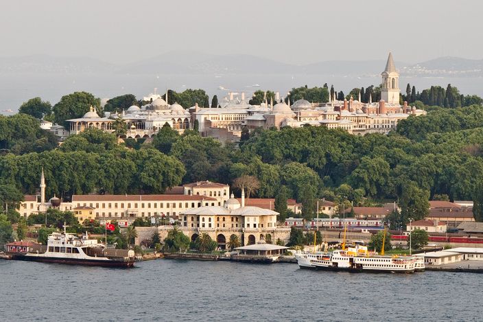 Topkapı Palace spread along the top of its wooded promontory, seen from the water with ferries moving below it