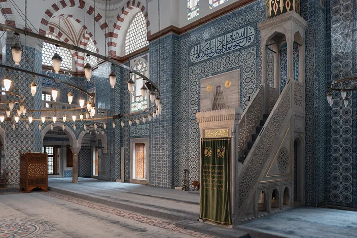 The tiled interior of the Rüstem Pasha Mosque: İznik panels in blue and red covering the walls and piers around a slender white minbar