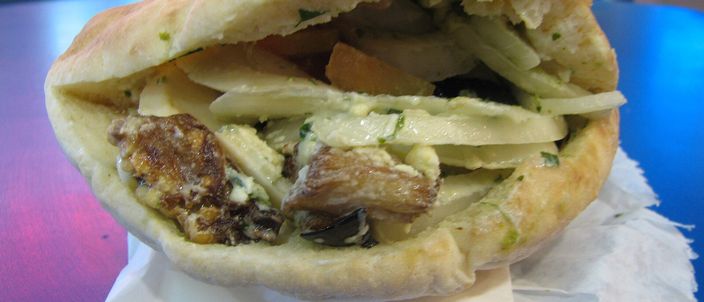 A sabich: a pita split and packed with fried aubergine, egg, sliced potato and chopped salad, standing upright on white napkins on a table.