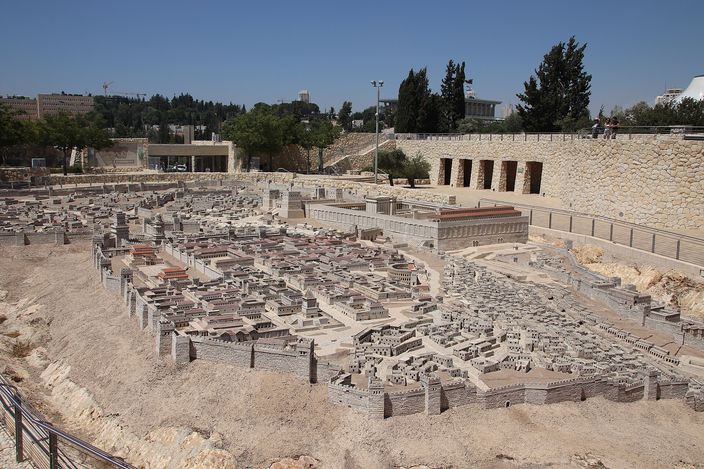 The open-air Model of Jerusalem in the Second Temple period at the Israel Museum: a large outdoor scale model of the ancient city in pale stone and terracotta roofs, laid out in a shallow excavated bowl with a colonnaded temple platform and its retaining wall at the right, trees and museum buildings behind.