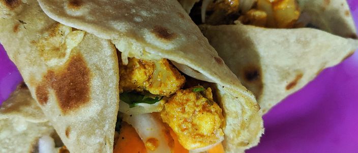 Two kathi rolls cut open on a plate, showing a spiced filling wrapped in a layered, griddled paratha.