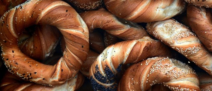 A close pile of golden-brown braided ring breads, their twisted strands crusted with poppy seeds and sesame.