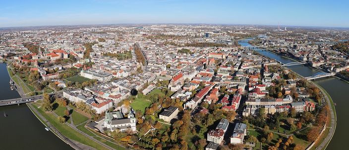 Kraków's historic centre from the air: the dense grid of the Old Town ringed by the green belt of the Planty, with the Vistula curving past on the right and the flat Polish plain beyond.