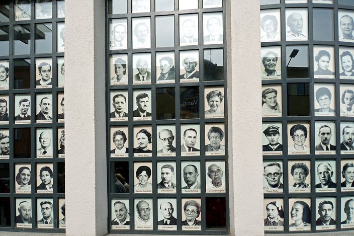 A window wall at Oskar Schindler's enamel factory in Kraków, every pane filled with black-and-white portrait photographs of the Jewish workers who survived, each face captioned with the person's name.