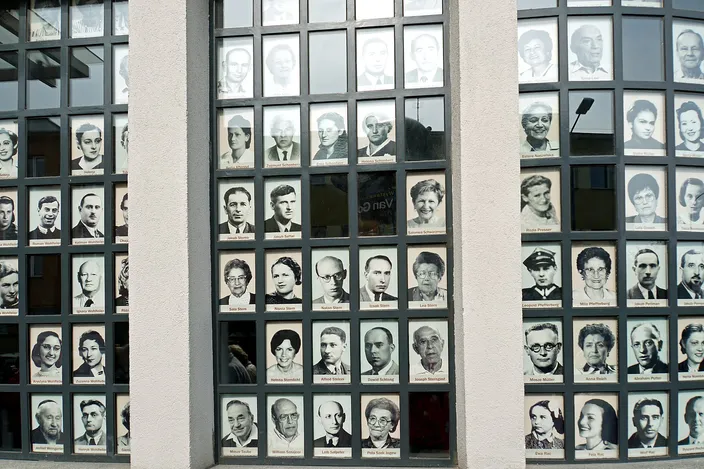 A window wall at Oskar Schindler's enamel factory in Kraków, every pane filled with black-and-white portrait photographs of the Jewish workers who survived, each face captioned with the person's name.