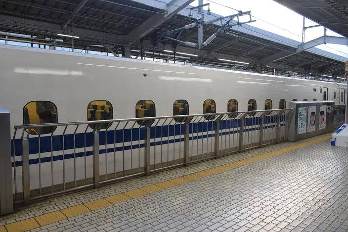 A white and blue Shinkansen standing at a Kyoto Station platform behind low platform screen doors, tiled platform empty in the foreground