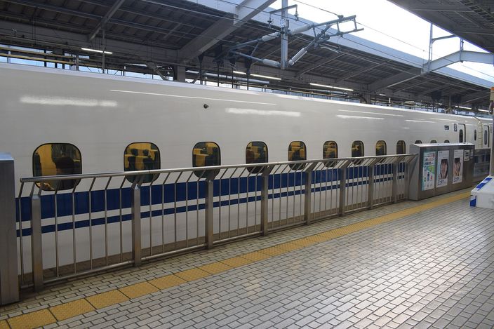 A white and blue Shinkansen standing at a Kyoto Station platform behind low platform screen doors, tiled platform empty in the foreground
