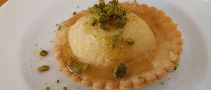 A fried pastry tart filled with melted cheese, drizzled with honey and topped with crushed pistachio, plated at a restaurant.