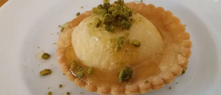 A fried pastry tart filled with melted cheese, drizzled with honey and topped with crushed pistachio, plated at a restaurant.