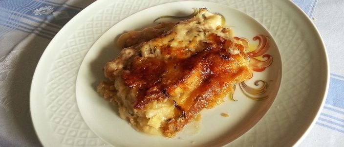 A plated slice of zuppa gallurese on an ornate ceramic dish, showing the golden-brown baked crust over layers of soaked bread and cheese.