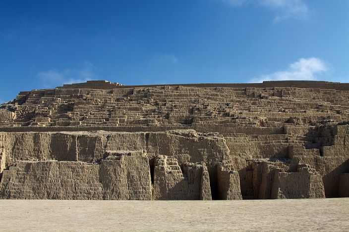 The stepped adobe and clay pyramid of Huaca Pucllana rising against a clear blue sky, its eroded terraced walls filling the frame.