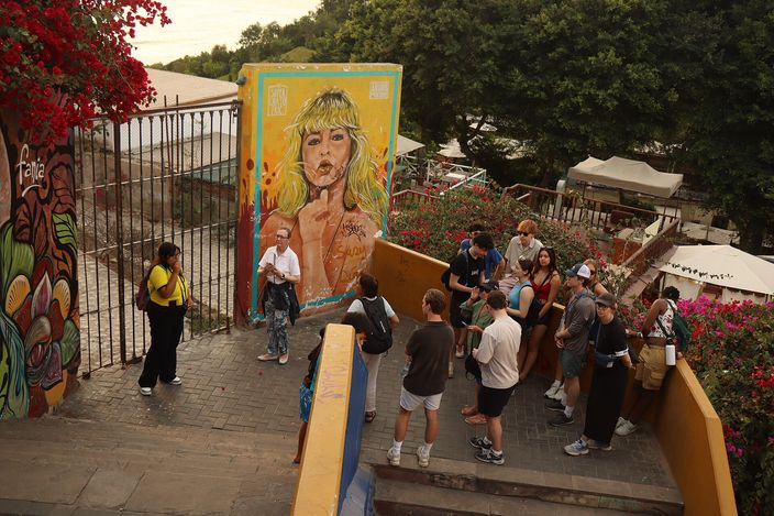 A large mural of a woman's face on a stairway wall in Barranco, with red bougainvillea in bloom and a group of tourists gathered on the steps at dusk.