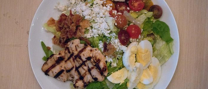 A plate of chopped salad with grilled chicken, halved hard-boiled eggs, tomato, bacon and crumbled cheese