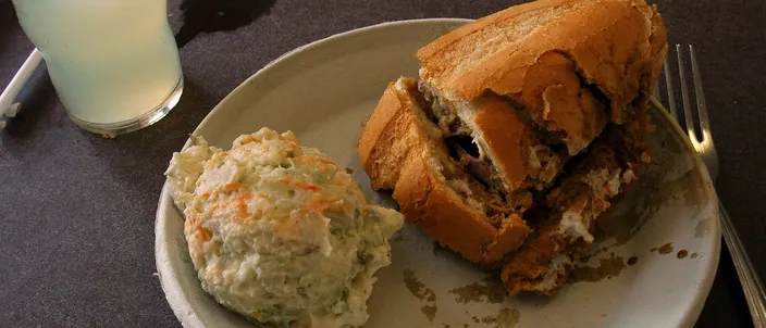 A French dip sandwich on a crusty roll served on a plate with potato salad and a glass of lemonade at a Los Angeles lunch counter.