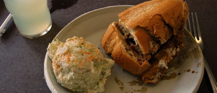 A French dip sandwich on a crusty roll served on a plate with potato salad and a glass of lemonade at a Los Angeles lunch counter.